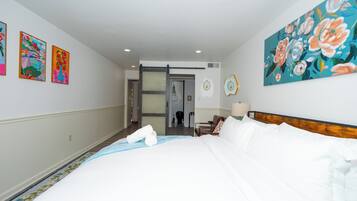 A hotel room with a bed, a door, a painting, and a wall-mounted picture frame.