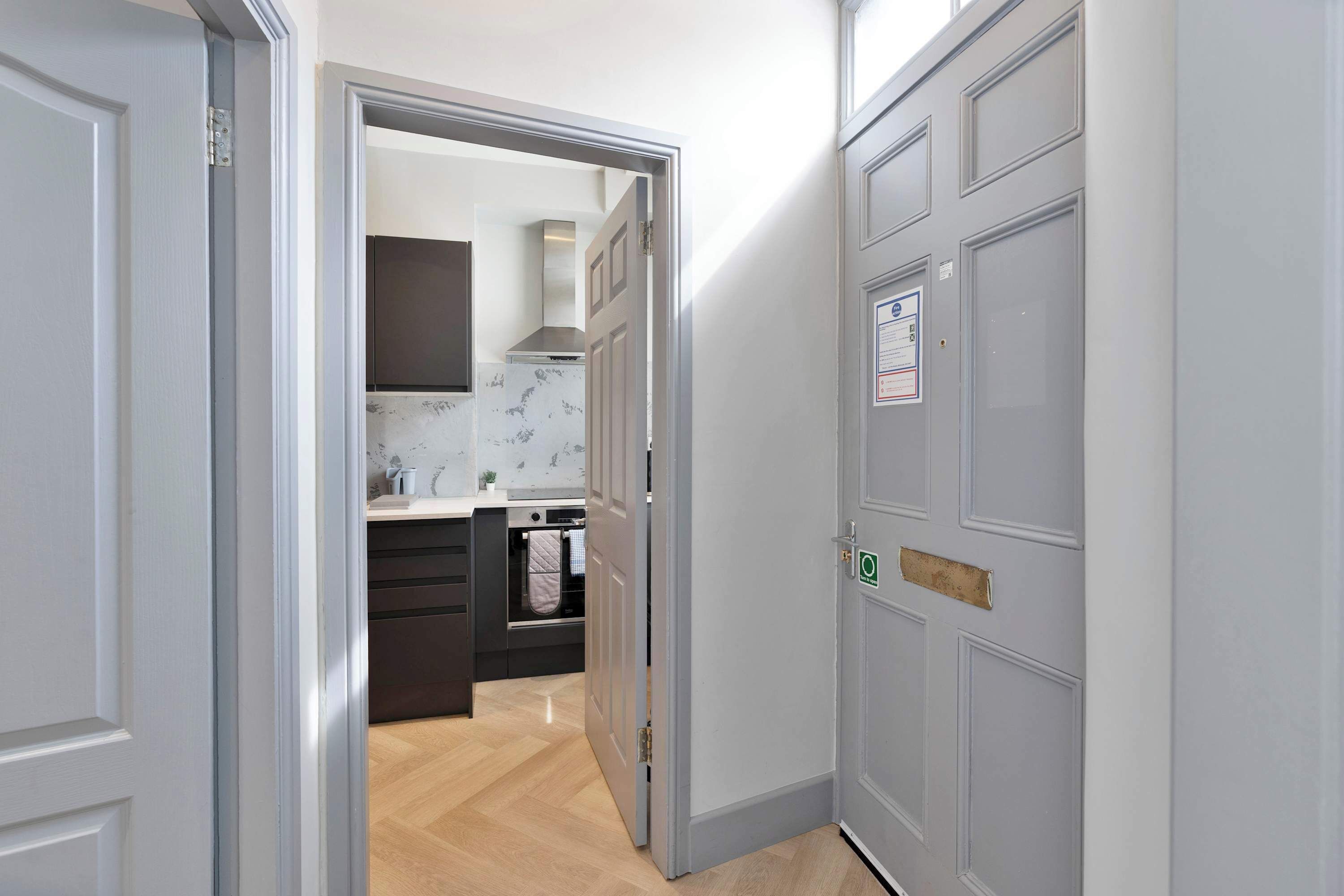 A hallway leading to a kitchen with a modern design, featuring a stainless steel range hood and a built-in oven.