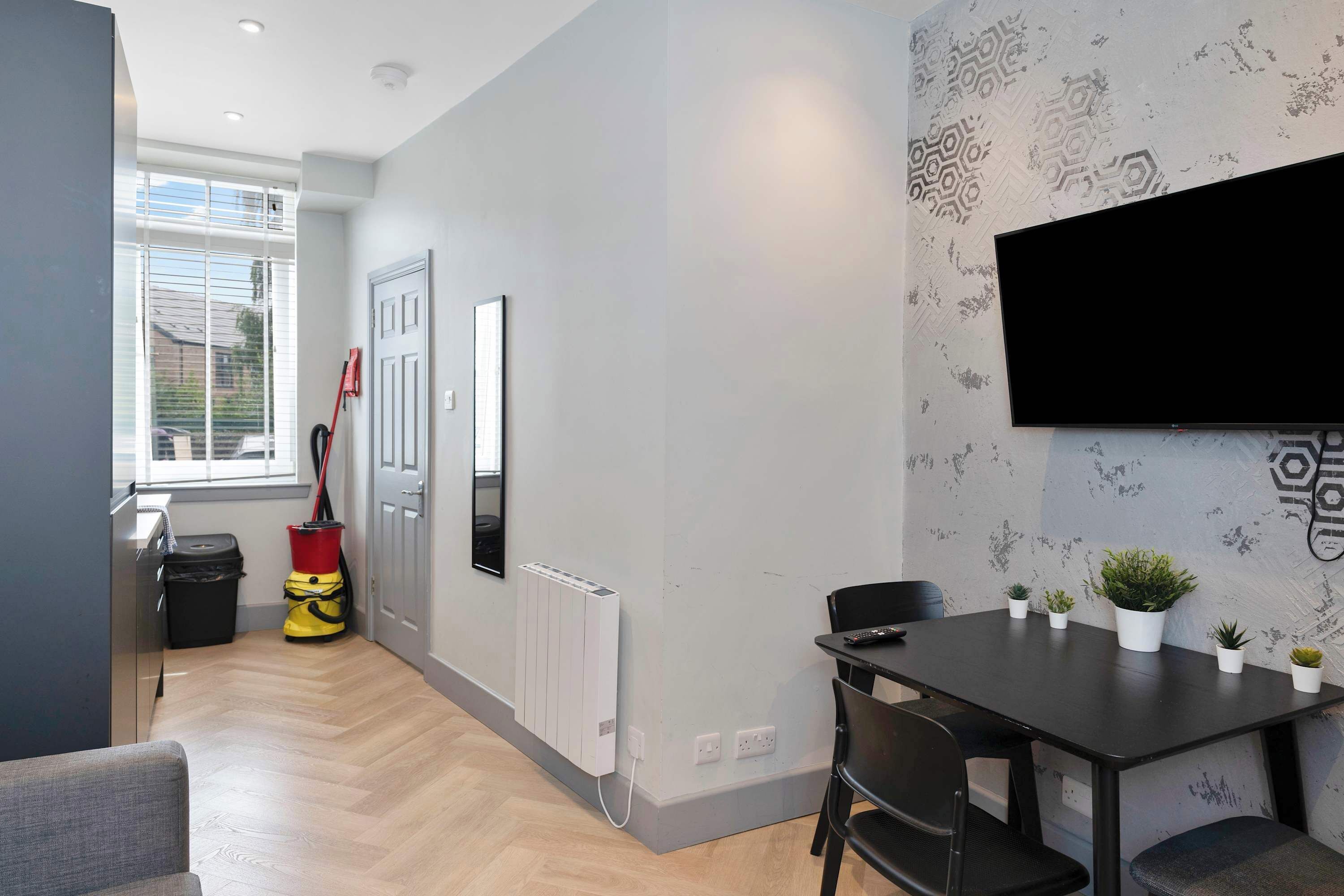 A modern living room with a dining area, a large window, a radiator, and a mounted TV.