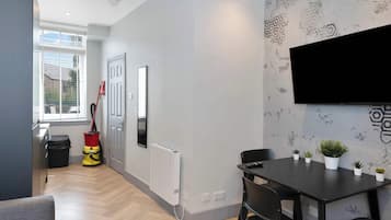 A modern living room with a dining area, a large window, a radiator, and a mounted TV.