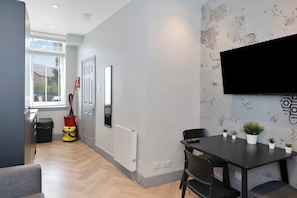 A modern living room with a dining area, a large window, a radiator, and a mounted TV. - Edinburgh Leith 1BR, Free Parking, Workspace (Edinburgh)