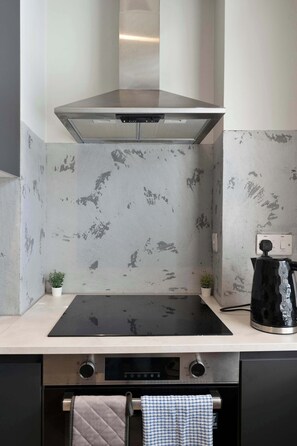 A kitchen with a black induction cooktop, a stainless steel range hood, and a coffee maker on the counter. - Edinburgh Leith 1BR, Free Parking, Workspace (Edinburgh)