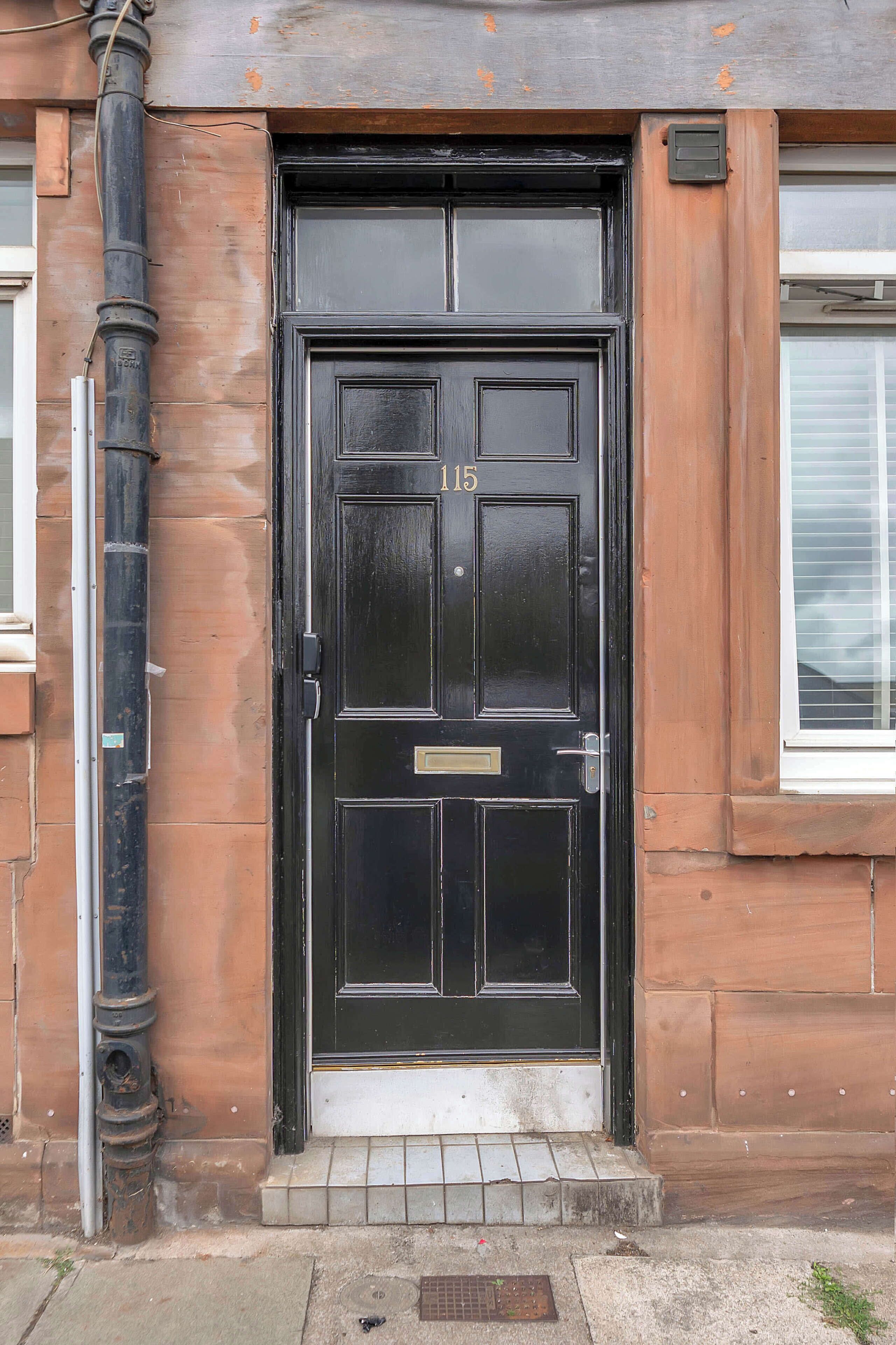 A black front door with the number 115, a metal handle, and a small step leading up to it.