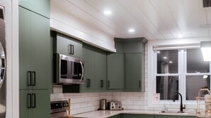 A modern kitchen with green cabinets, a stainless steel microwave, and a large island with a marble countertop. - The Lodge, Algonquin Woods (Perry)