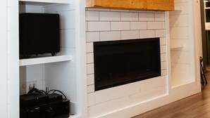 A fireplace with a TV above it, built into a white wall with shelves below. - The Lodge, Algonquin Woods (Perry)