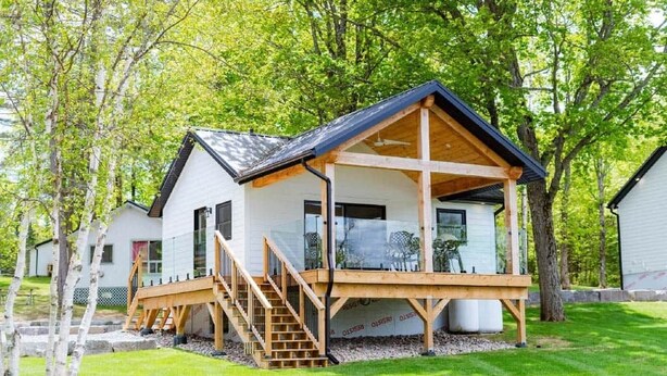 A single-story wooden cabin with a balcony, surrounded by trees. - Maple Haven, Algonquin Woods (Perry)