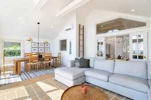 A spacious living area with a large grey sofa, a wooden dining table with chairs, and a high ceiling with exposed beams. - Beach House on the Dunes (Norfolk County)