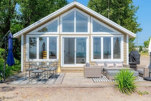 A modern house with a large glass door, outdoor seating, and a patio area. - Beach House on the Dunes (Norfolk County)