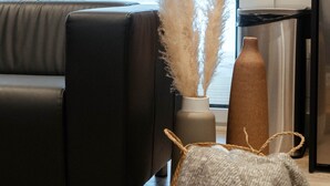 En moderne stue med en sort sofa, en vase med pampasgræs, en flettet kurv og en høj vase.