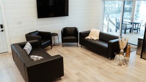 En moderne stue med et fladskærms-tv, to sofaer, et sofabord og en stor skydedør, der fører ud til en terrasse.