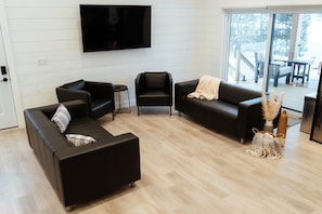 Ein modernes Wohnzimmer mit einem Flachbildfernseher, zwei Sofas, einem Couchtisch und einer großen Schiebeglasdoor zu einer Terrassenanlage.