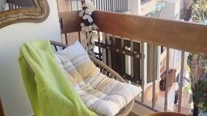 A balcony with a wicker chair, a small round table with a vase, and a view of neighboring buildings. - Marbella Sky Retreat el Nido Suite (Marbella)