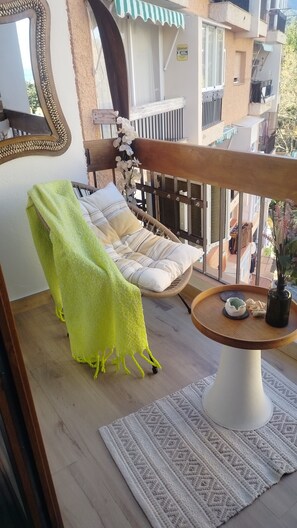 A balcony with a wicker chair, a small round table with a vase, and a view of neighboring buildings. - Marbella Sky Retreat el Nido Suite (Marbella)