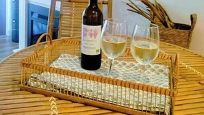 A round wooden table with a woven tray holding a wine bottle and two glasses, a wicker chair, and a fireplace in the background. - Marbella Sky Retreat el Nido Suite (Marbella)