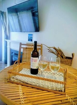 A round wooden table with a woven tray holding a wine bottle and two glasses, a wicker chair, and a fireplace in the background. - Marbella Sky Retreat el Nido Suite (Marbella)