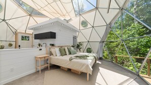 Ein modernes Schlafzimmer mit Bett, Nachttisch und Blick ins Grüne durch ein großes Fenster.