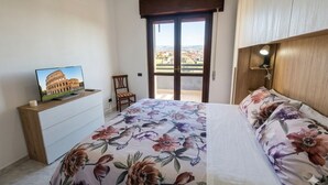 Une chambre à coucher avec un lit, un téléviseur posé sur une commode en bois, une chaise et un balcon avec vue.