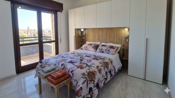Une chambre avec un lit, un banc en bois, une armoire et un balcon avec vue.