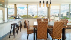 A modern kitchen with a dining area, large windows, and a view of buildings. - 2 Br condo with Rooftop Pool - Doca 303 (Playa del Carmen)