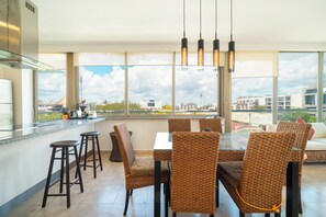 A modern kitchen with a dining area, large windows, and a view of buildings. - 2 Br condo with Rooftop Pool - Doca 303 (Playa del Carmen)