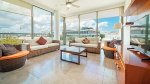 A spacious living area with a large window, a ceiling fan, and a flat-screen TV. - 2 Br condo with Rooftop Pool - Doca 303 (Playa del Carmen)