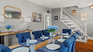 A dining room with a wooden table, blue upholstered chairs, and a vase with blue flowers. - NEW - Sleeps 12, Fun Yard, Fire Pit Walk to Water! (Bristol)