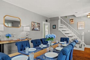 A dining room with a wooden table, blue upholstered chairs, and a vase with blue flowers. - NEW - Sleeps 12, Fun Yard, Fire Pit Walk to Water! (Bristol)