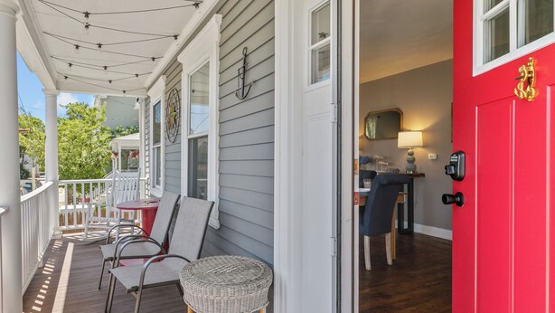 A porch with chairs, a wicker basket, and a red door leading to a room with a lamp and a mirror. - NEW - Sleeps 12, Fun Yard, Fire Pit Walk to Water! (Bristol)