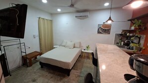 A compact room with a bed, a small table, a TV, and a kitchenette area. - Dager Cottage (Mérida,)