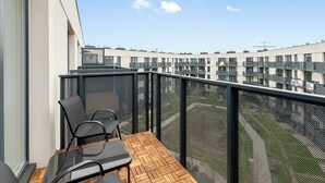 Un balcón con una mesa y sillas de madera, barandilla de malla y vista a un edificio de varios pisos.