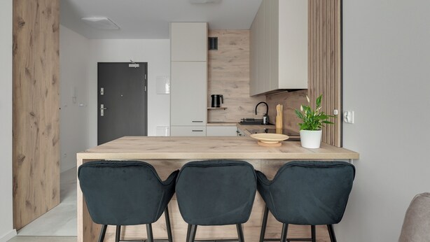 Una cocina moderna con una isla de madera, sillas negras y una planta en maceta.