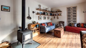A cozy living room with a wood-burning stove, a blue sofa, a red sofa, and wooden shelves with various items. - The Farmhouse at Deadman Acres (Thompson-Nicola)