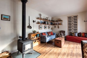 A cozy living room with a wood-burning stove, a blue sofa, a red sofa, and wooden shelves with various items. - The Farmhouse at Deadman Acres (Thompson-Nicola)