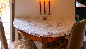 A dining table with a crocheted tablecloth, three lit candles, and a framed painting on the wall. - The Farmhouse at Deadman Acres (Thompson-Nicola)