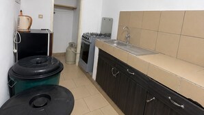 A kitchen with a stove, oven, sink, and a trash bin.