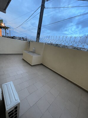 A balcony with tiled flooring, a white bench, and a wall with a barbed wire fence. - Furnished apartment in a residential neighborhood (bingerville)