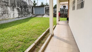 A corridor with a tiled floor, a grassy area with a low wall, and a building with barred windows.
