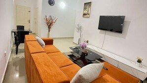 A modern living room with a sofa set, a dining table, a TV mounted on the wall, and a clock on the wall.