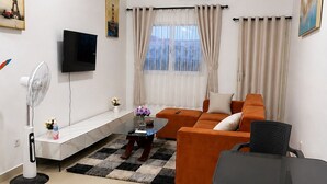 A modern living room with a sofa, a TV, a fan, and a dining table.