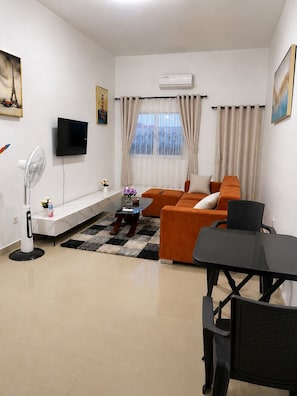 Un salon moderne avec un canapé, un téléviseur, un ventilateur et une table à manger.