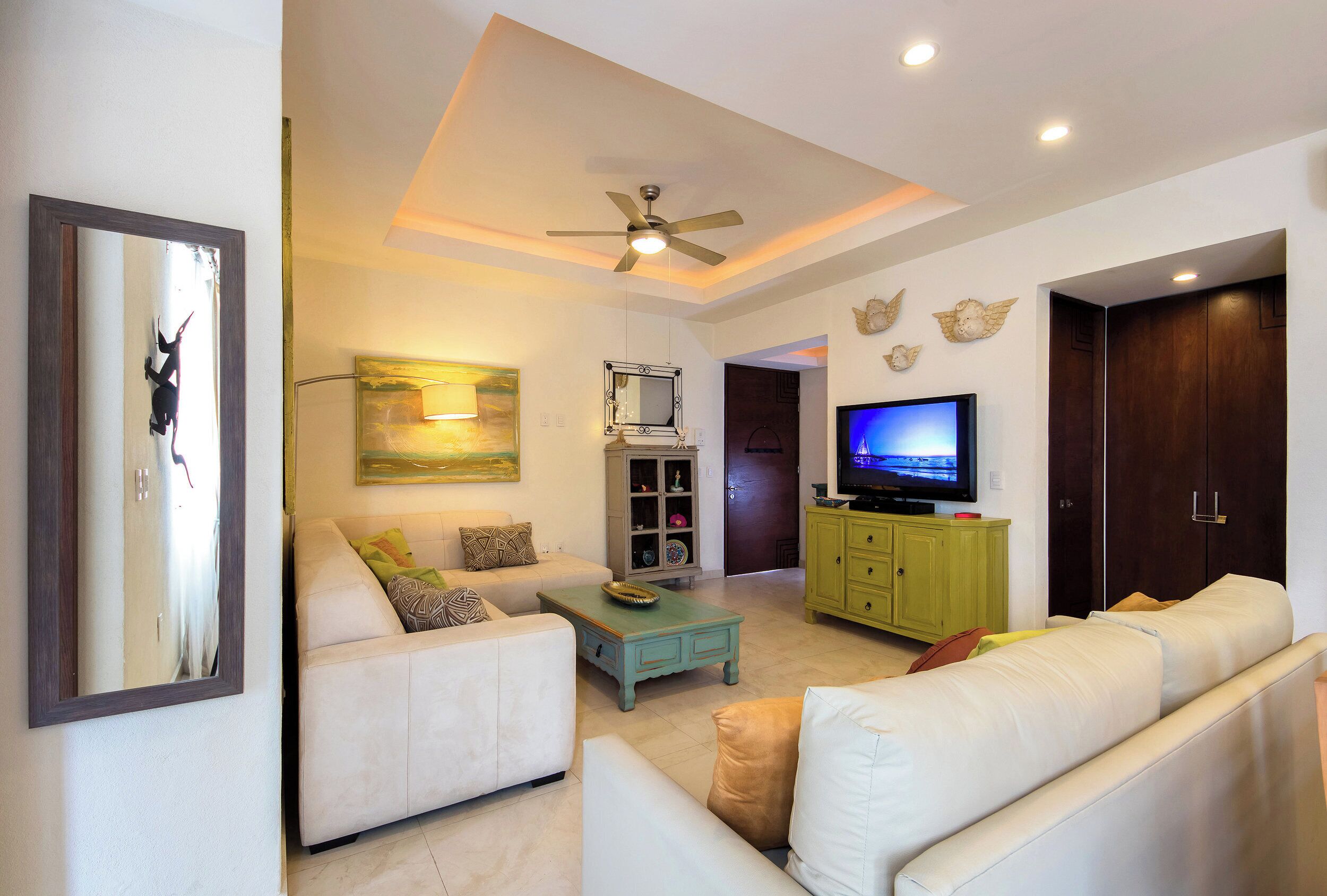 A living room with a sofa, a coffee table, a television, and a ceiling fan.