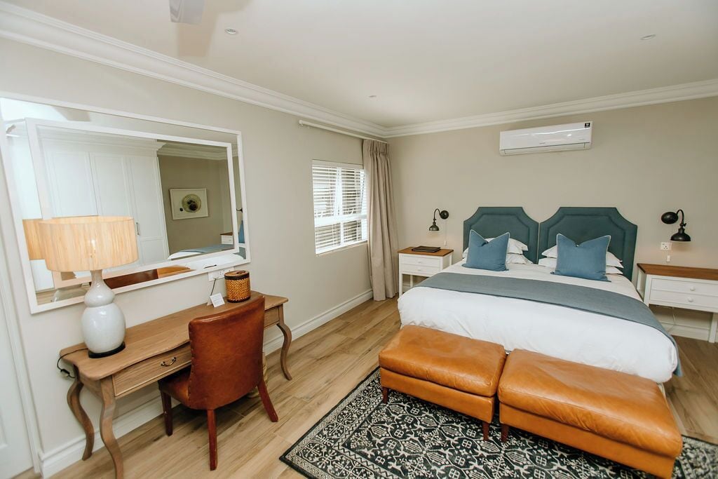 A bedroom with a bed, a desk, a chair, a mirror, and a bedside table.