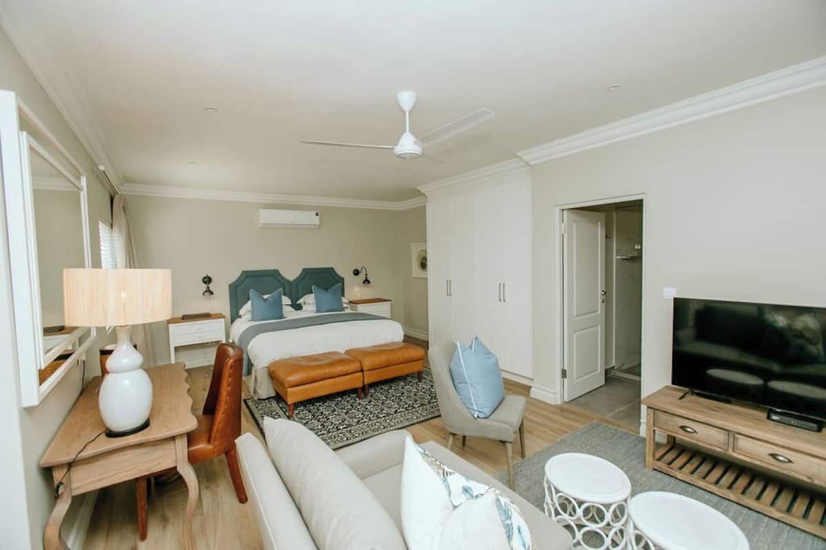 Habitación de hotel con cama, escritorio con lámpara, televisor, sofá, sillón y ventilador de techo.