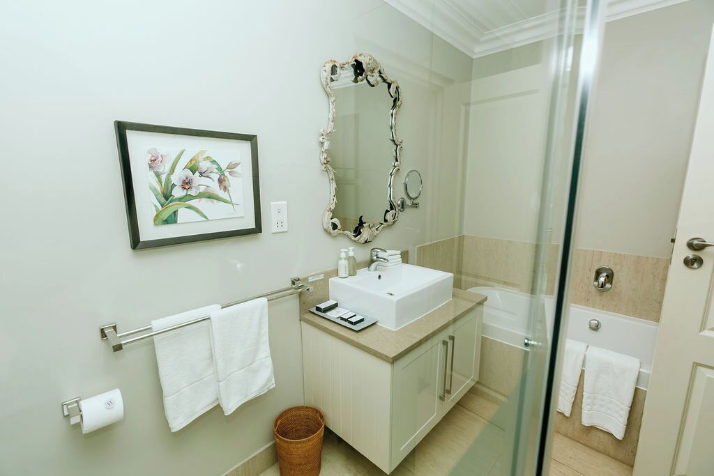 Casa de banho com lavatório, espelho, quadro floral emoldurado e cabine de duche em vidro.