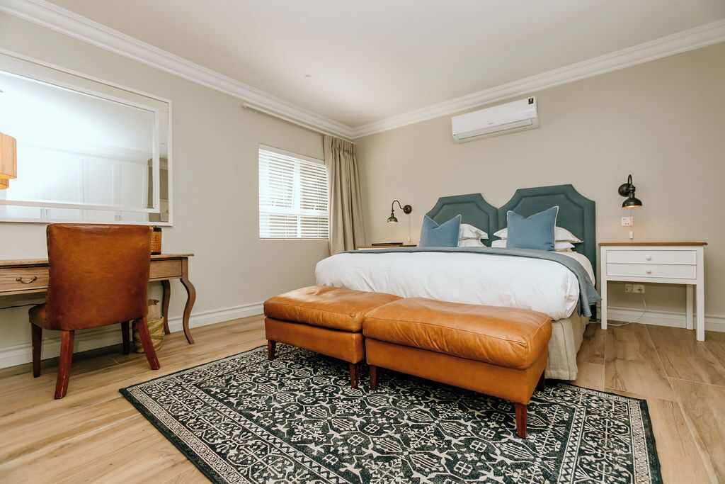 Een slaapkamer met een bed, een bureau, een stoel, een bankje en een kamerbreed tapijt met een patroon.