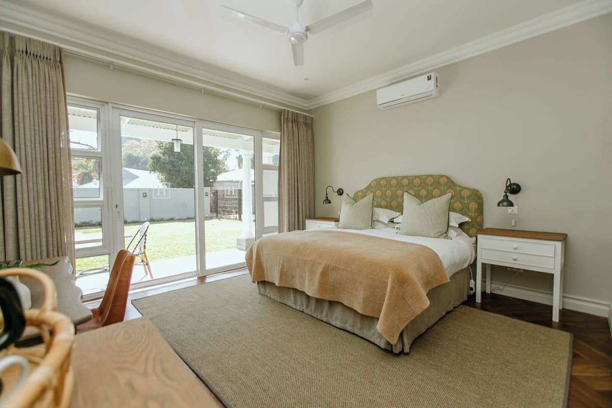 Un dormitorio con cama, mesitas de noche, ventilador de techo y vistas a través del ventanal.