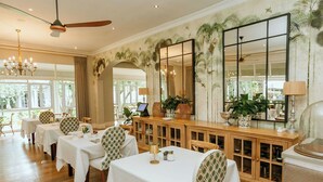 Un comedor con mesas y sillas, un aparador de madera con objetos decorativos y un espejo grande.