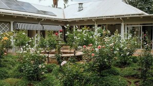 Una casa con porche cubierto, jardín de rosas y paneles solares en el techo.