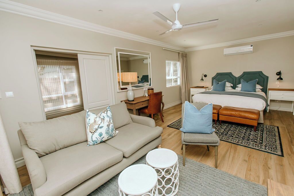 A hotel room with a bed, a sofa, a desk, a chair, a ceiling fan, and a window with curtains.