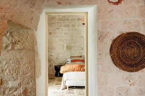 A rustic room with a stone wall, a bed with a striped pillow, and a woven rug. - Trullo Badra, in the countryside between Alberobello and Locorotondo (Puglia)